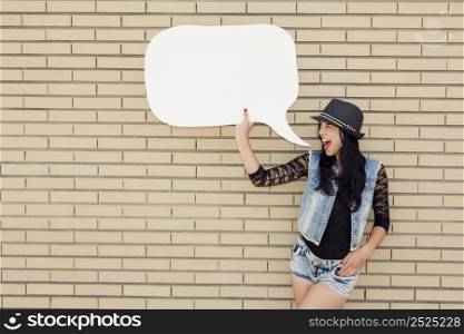 Beautiful and young teenager holding a thought balloon, in front of a brick wall