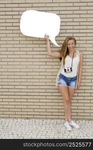 Beautiful and young teenager holding a thought balloon, in front of a brick wall