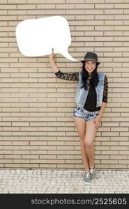 Beautiful and young teenager holding a thought balloon, in front of a brick wall