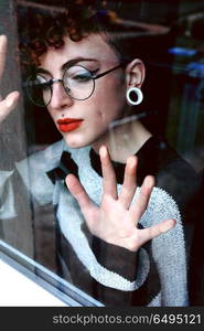 Beautiful and youthful redhead woman looking through a window