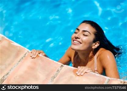 Beautiful Arab woman relaxing in swimming pool with eyes closed. Girl with healthy tanned skin and wet hair enjoying Summer Sun.. Beautiful Arab woman relaxing in swimming pool.
