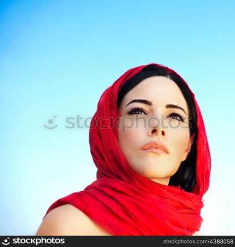 Beautiful arabic woman wearing red scarf, traditional muslim clothes, latest fashion design, stylish female portrait over blue natural background with copy space, soft focus