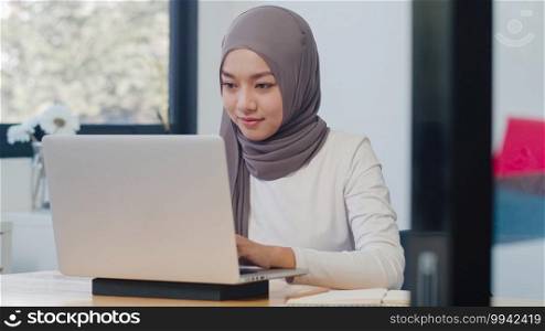 Beautiful Asia muslim lady casual wear working using laptop in modern new normal office. Working from home, remotely work, self isolation, social distancing, quarantine for coronavirus prevention.