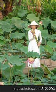 Beautiful asia women wearing white white traditional Vietnam dress  Ao Wai  and Vietnam farmer’s hat and standing on wooden boat in flower lotus lake. Her hands holding lotus flowers.