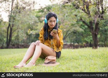 Beautiful Asian Bohemian girl with yellow vintage dress chat and listen online music by smartphone or mobile phone in park. Female hipster play social media, watch video, shop online in garden.
