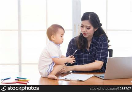 Beautiful Asian business mom is using laptop, smiling, spending time with cute baby girl at home, Single mother take care adorable child kid, working on technology computer cardboard box background