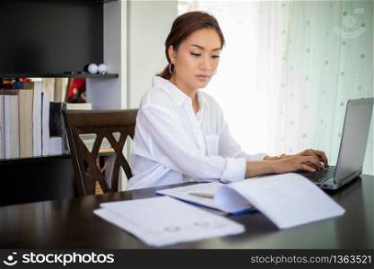 Beautiful Asian business women checking document and using notebook working from home for social distance and self responsibility concept