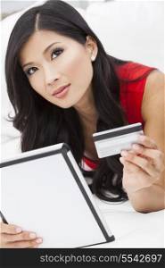 Beautiful Asian Chinese woman using a credit card to shop on the internet with a tablet computer