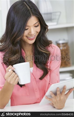 Beautiful Asian Chinese Woman Using Tablet Computer and drinking tea or coffee at home in her kitchen