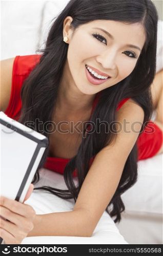 Beautiful Asian Chinese woman wearing red dress using tablet computer on line to surf the web &amp; internet