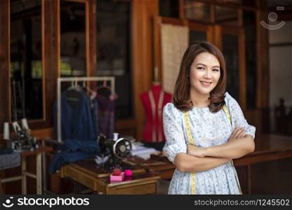 Beautiful asian dressmaker in workroom .designer woman keeping arms crossed and looking at camera with smile while standing in workshop. Beautiful asian dressmaker in workroom