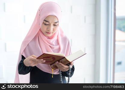 Beautiful asian female Muslim woman in modern kurung and hijab, read quran.