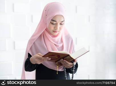 Beautiful asian female Muslim woman in modern kurung and hijab, read quran.