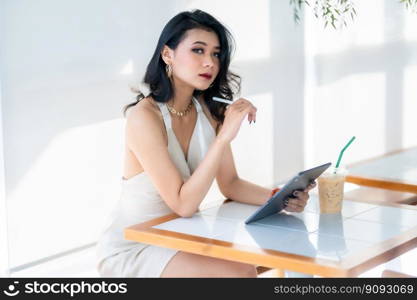 beautiful asian freelance Success people business woman fashion model in summer white sleeveless dress using casual working with tablet for browsing internet, chatting and blogging in coffee shop.