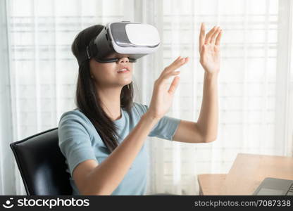 Beautiful Asian girl are looking through vr glasses to play games at home, woman is using glasses with virtual reality headsets at the desk