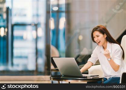 Beautiful Asian girl celebrate with laptop, success happy pose. E-commerce, university education, internet technology, or startup small business concept. Modern office or living room with copy space