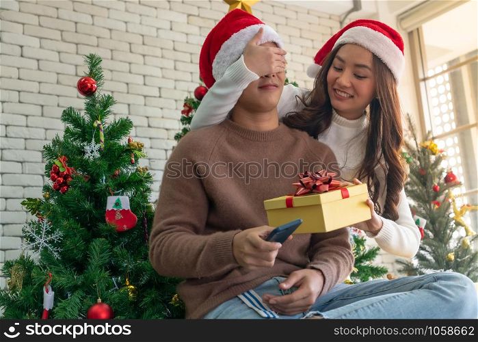 beautiful asian girl give surprise christmas gift to her boyfriend in Christmas holiday season greeting.