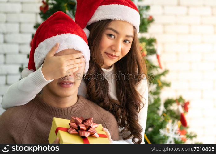 beautiful asian girl give surprise christmas gift to her boyfriend in Christmas holiday season greeting.