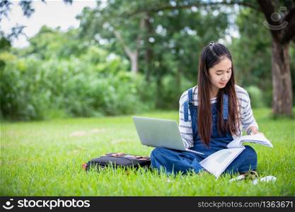 beautiful Asian girl student holding books and smiling at camera and learning and education concept on park in summer for relax time