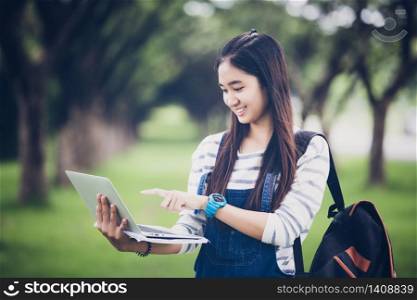 beautiful Asian girl student holding books and smiling at camera and learning and education concept on park in summer for relax time at sunset with a warm light