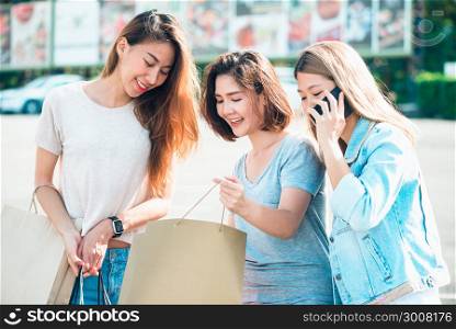 Beautiful asian girls holding shopping bags, using a smart phone and smiling while standing outdoors. Shopping and tourism concept. A picture of a group of happy asian friends women shopping in city.