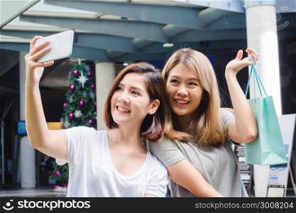 Beautiful asian girls holding shopping bags, using a smart phone selfie and smiling while standing outdoors. Shopping and tourism concept. Picture group of happy asian friends women shopping in city.