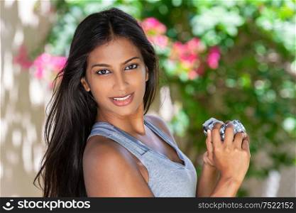 Beautiful Asian Indian girl or young woman photographer happy taking pictures or photographs outside with a retro digital camera surrounded by flowers