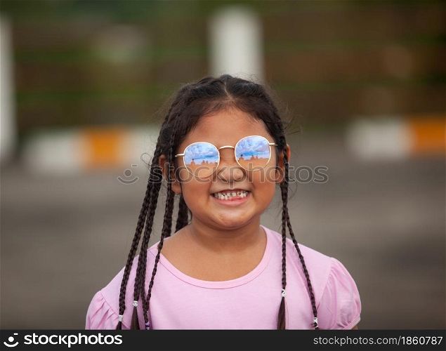 Beautiful Asian kid with long hair wearing glasses smiles happily after her baby teeth fall out.