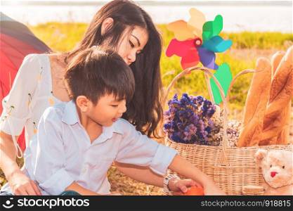 Beautiful Asian mother and son doing picnic and in Easter summer party on meadow near lake and mountain. Holiday and Vacation. People lifestyle and Happy family life concept. Thai person