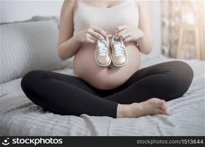 Beautiful asian pregnant woman expecting her baby with small shoes