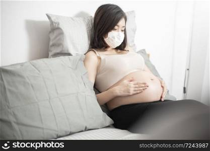 Beautiful asian pregnant woman is wearing protective mask in her home , Coronavirus protection concept