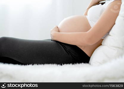 Beautiful Asian pregnant woman lie on bed and use hand touch belly with carefully emotion. Concept of good healthy activity for mother and support growth of baby in womb of people.