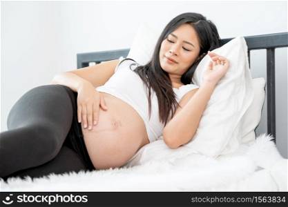 Beautiful Asian pregnant woman lie with relax position and use one hand touch her belly. Concept of good healthy activity for mother and support growth of baby in womb of people.