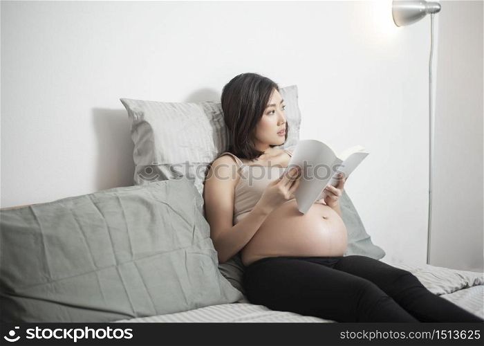Beautiful asian pregnant woman lying on her bed and reading a book