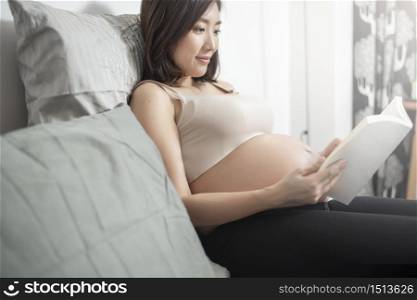 Beautiful asian pregnant woman lying on her bed and reading a book