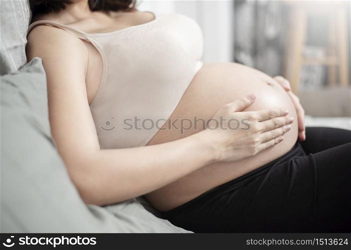 Beautiful asian pregnant woman lying on her bed, touching big belly