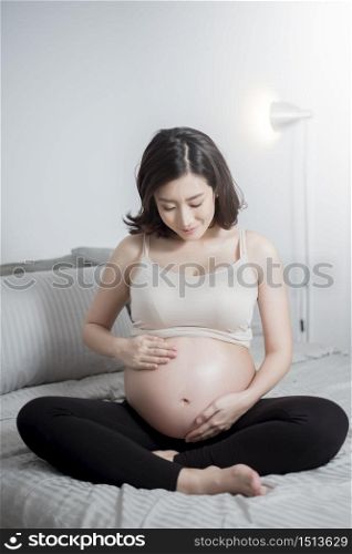 Beautiful asian pregnant woman sit on bed and touching her belly