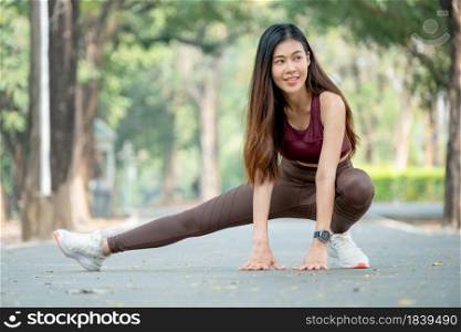 Beautiful Asian sport woman stretching right legs on road of park or garden also smile from relaxation after exercise in the morning.