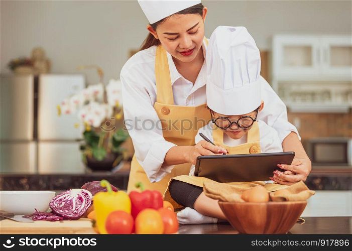 Beautiful Asian woman and cute little boy prepare online shopping and listing ingredient for cooking in kitchen at home with tablet. People lifestyles and Family. Homemade food and ingredient concept.