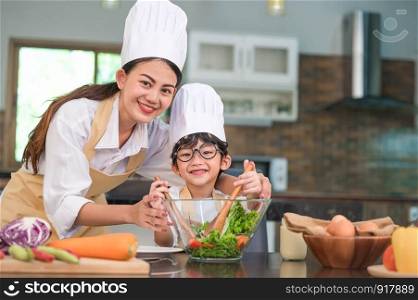 Beautiful Asian woman and cute little boy with eyeglasses prepare to cooking in kitchen at home. People lifestyles and Family. Homemade food and ingredients concept. Two Thai people looking at camera