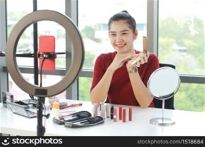 Beautiful Asian woman blogger hand holding Powder puff box and recording on red smartphone for make up tutorial video in Cosmetics Vlog website. Youtber and Marketing in social media concept.