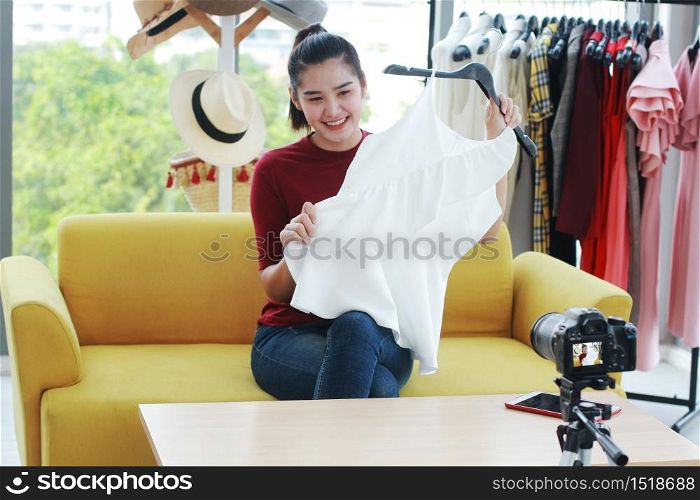 Beautiful Asian woman blogger recording on video Dslr Camera for selling White dress online shopping on Vlog website. Marketing in social media concept.