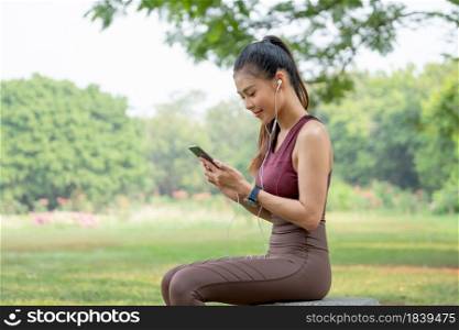 Beautiful Asian woman enjoy to use mobile phone with relaxation after exercise in park or garden.