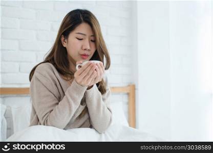 Beautiful Asian woman enjoying warm coffee on bed in her bedroom. Beautiful Asian woman enjoying warm coffee on bed in her bedroom. Relaxation in bed. Beautiful Asian female wearing comfortable sweater holding a cup of coffee. lifestyle Asian woman at home concept.