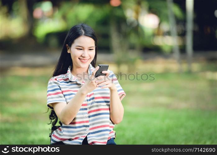 Beautiful asian woman happy and smiling / Young girls student woman playing using smartphone in garden park outdoors