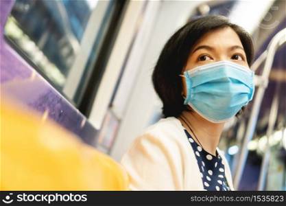 Beautiful Asian Woman in protective face mask for protection coronavirus or covid-19 or air pollution inside commuter train or metro. Young female travelling to work by underground with New normal