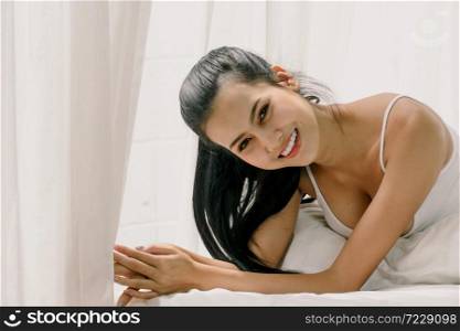 Beautiful asian woman in white dress just woke up and laying on the bed smile and happy. Sexy look in the morning time. Copy Space.