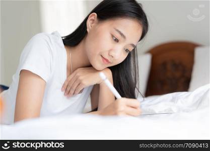 Beautiful Asian woman is drawing on the bed. Asian girl using tablet to learn to draw at her home.