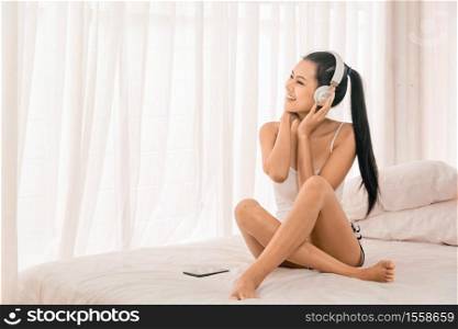 Beautiful asian woman just woke up and laying on the bed and listening music in the morning light. Song, Music, Relax , Gadget concept Copy Space.