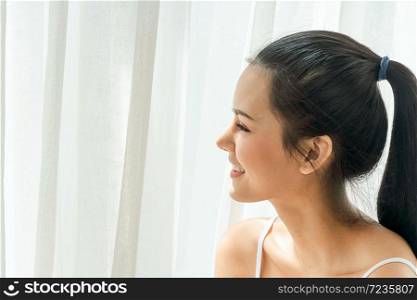 Beautiful asian woman just woke up and laying on the bed smile and looking outside. Sexy look in the morning time. Copy Space.